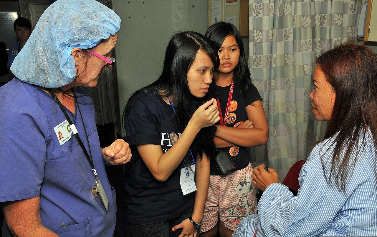 Language access is a clinical intervention rather than a courtesy — the trained interpreter sits beside the encounter while the nurse speaks to the patient, not about her.