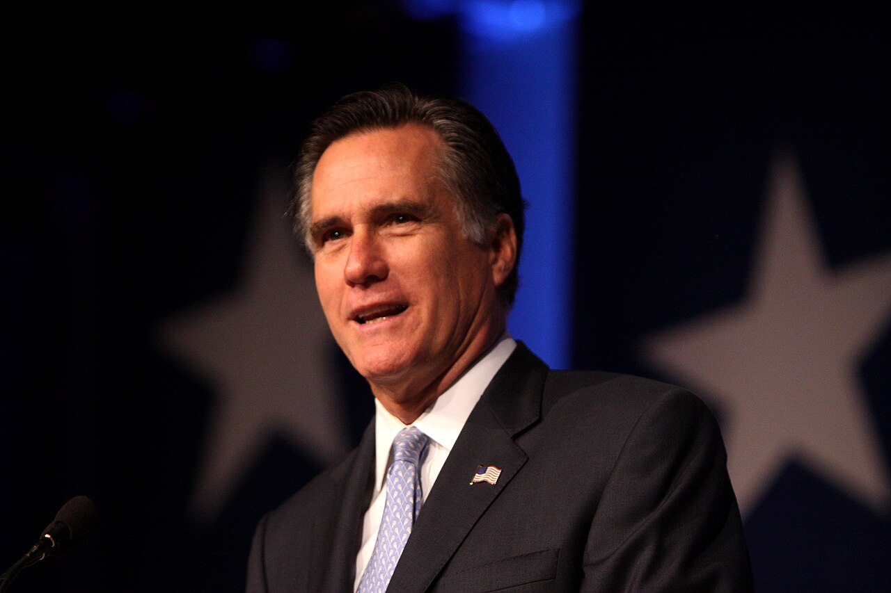 Close view of a person speaking into a microphone on a stand, mouth open mid-word, hands raised in a small gesture