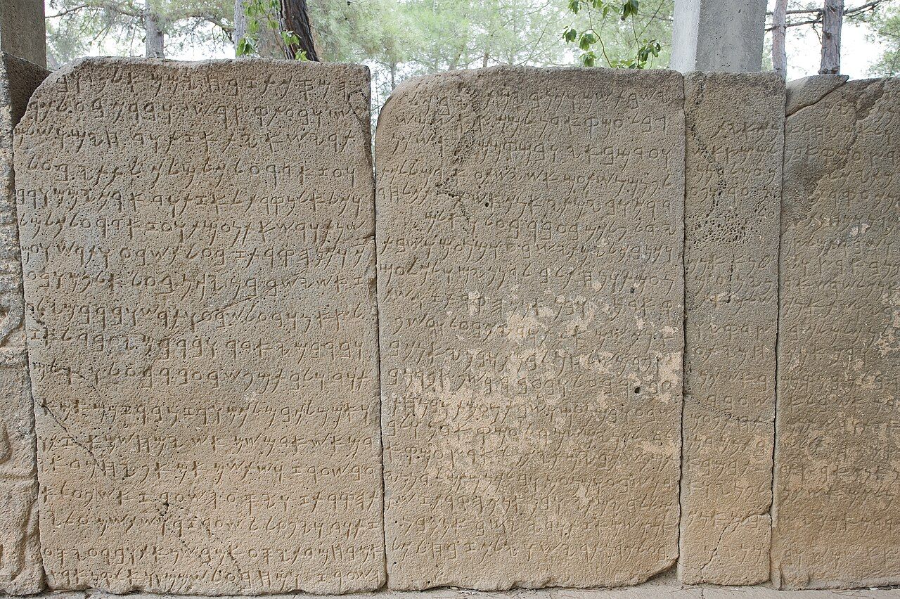 A stone inscription in early Phoenician alphabetic script, showing rows of simple angular consonant letters carved into the surface